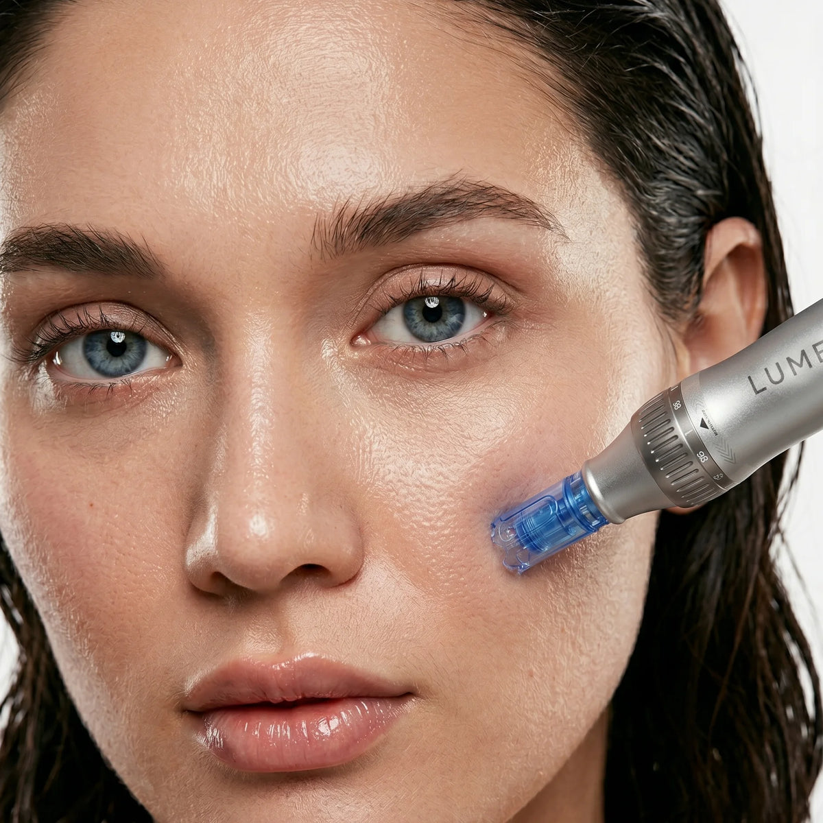 High-end, close-up beauty portrait of a woman with wet-look hair and radiant skin, precisely applying the silver LUMEPEN PRO microneedling pen cartridge to her cheek to treat acne scars, large pores, and uneven skin texture.